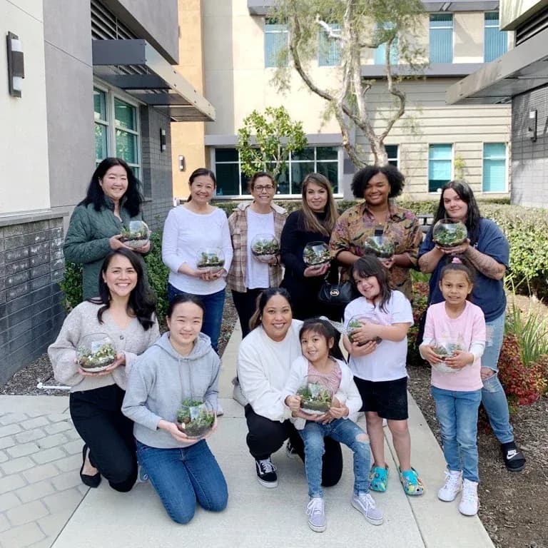 Adults and kids outdoors holding the terrariums they made at a workshop